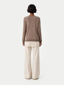 back view of a person wearing a brown sweater and white pants on a light gray background #color_taupe