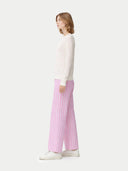 side view of a woman wearing a white top and pink striped pants on a white background #color_whisper-white