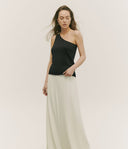 Woman wearing a black one-shoulder top and light-colored pants against a plain background