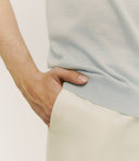 Person wearing a light blue sleeveless top and beige pants on a plain background