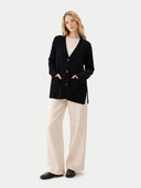Woman wearing a black cardigan with split hem and beige pants on a white background.