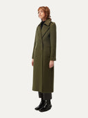 side view of a woman wearing a long double breasted green coat on a white background #color_avocado