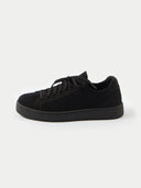 A side profile view of a low-top sneaker featuring a black-colored knit upper and matching laces. The shoe has a smooth suede-like heel counter and eyelet overlays in the same tone, all set against a thick white rubber midsole and a white background.#color_black