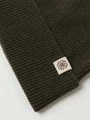 close up of a dark green ribbed beanie with a small brand logo on a light gray background #color_avocado