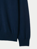 Close-up of a navy blue sweater sleeve on a light gray background. #color_navy-blue