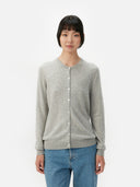 A woman wearing a gray cashmere crew neck cardigan with button closure, over a white top, paired with blue jeans. #color_dawn-blue