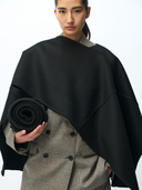 Person wearing a black poncho over a gray outfit holding a black blanket. #color_black