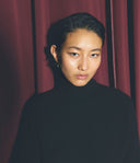 Person wearing a black turtleneck in front of a red curtain