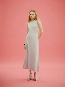 A woman standing on a pink background, wearing a lightweight cashmere silk dress with a V-neckline and sleeveless design. #color_ice-flow