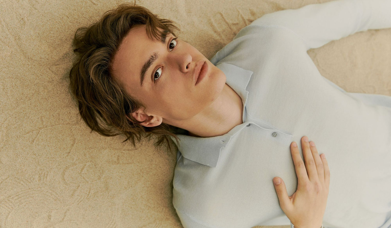Person lying on a beige surface wearing a light gray shirt.