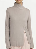 A front view of a person wearing the light beige knit turtleneck sweater, paired with pale pink trousers. The high ribbed collar features a slight overlap detail, and the vertical slit at the hem is visible on the left side.
#color_chateau-gray