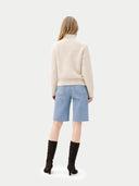 back view of a woman wearing a beige sweater and light blue denim shorts on a white background #color_off-white