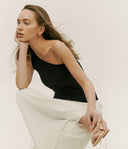 Woman wearing a black top and white pants against a plain background