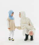 Two children wearing matching cream hooded outfits on a white background