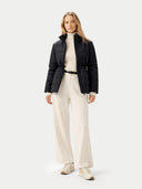 Woman wearing a black puffer jacket, white turtleneck, and cream pants on a white background #color_black