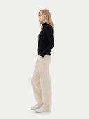 side view of a woman wearing a black zip-up cardigan and beige pants on a white background #color_black