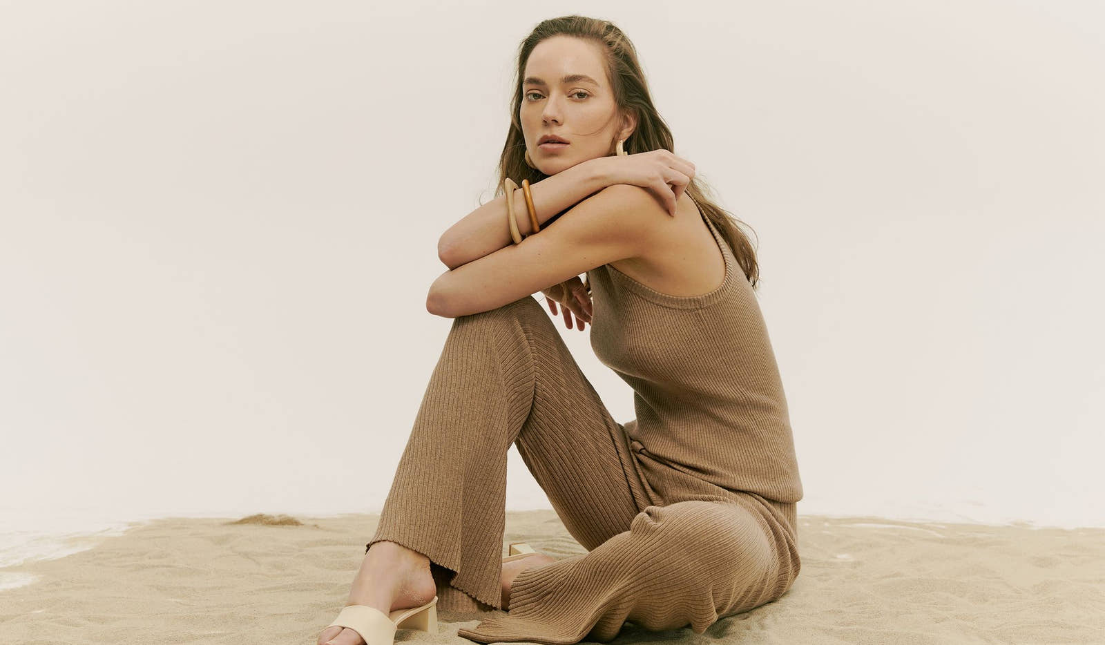 Woman in a brown outfit sitting on a wooden floor with a white background