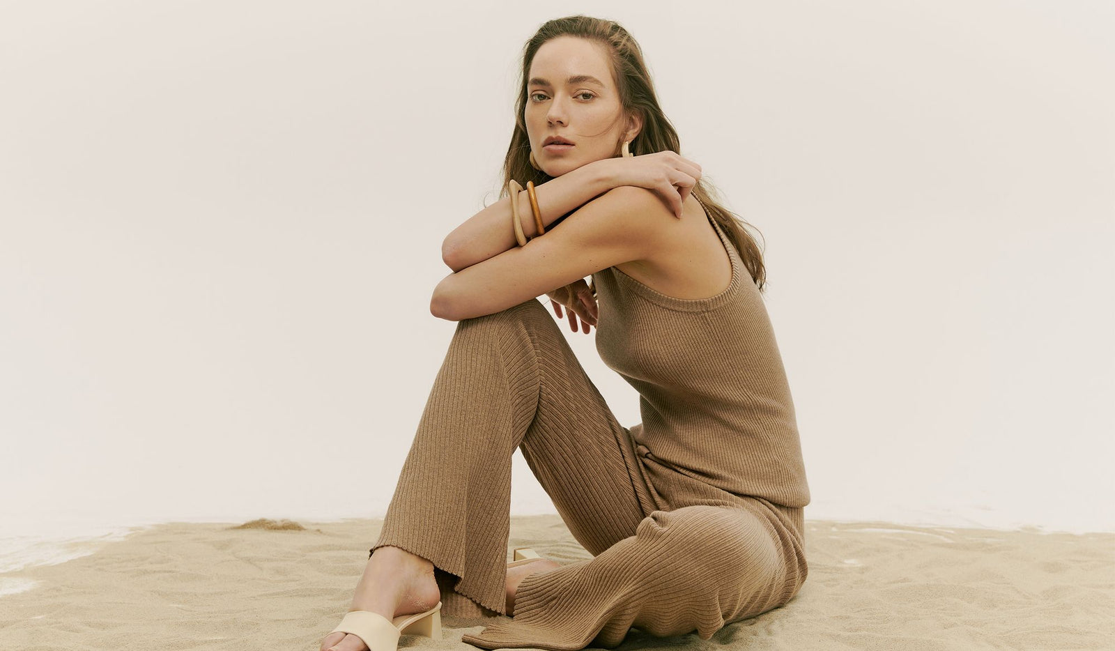 Woman in a brown outfit sitting on a wooden floor with a white background