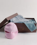 Pink beanie and blue sweater in an open brown box on a light gray background