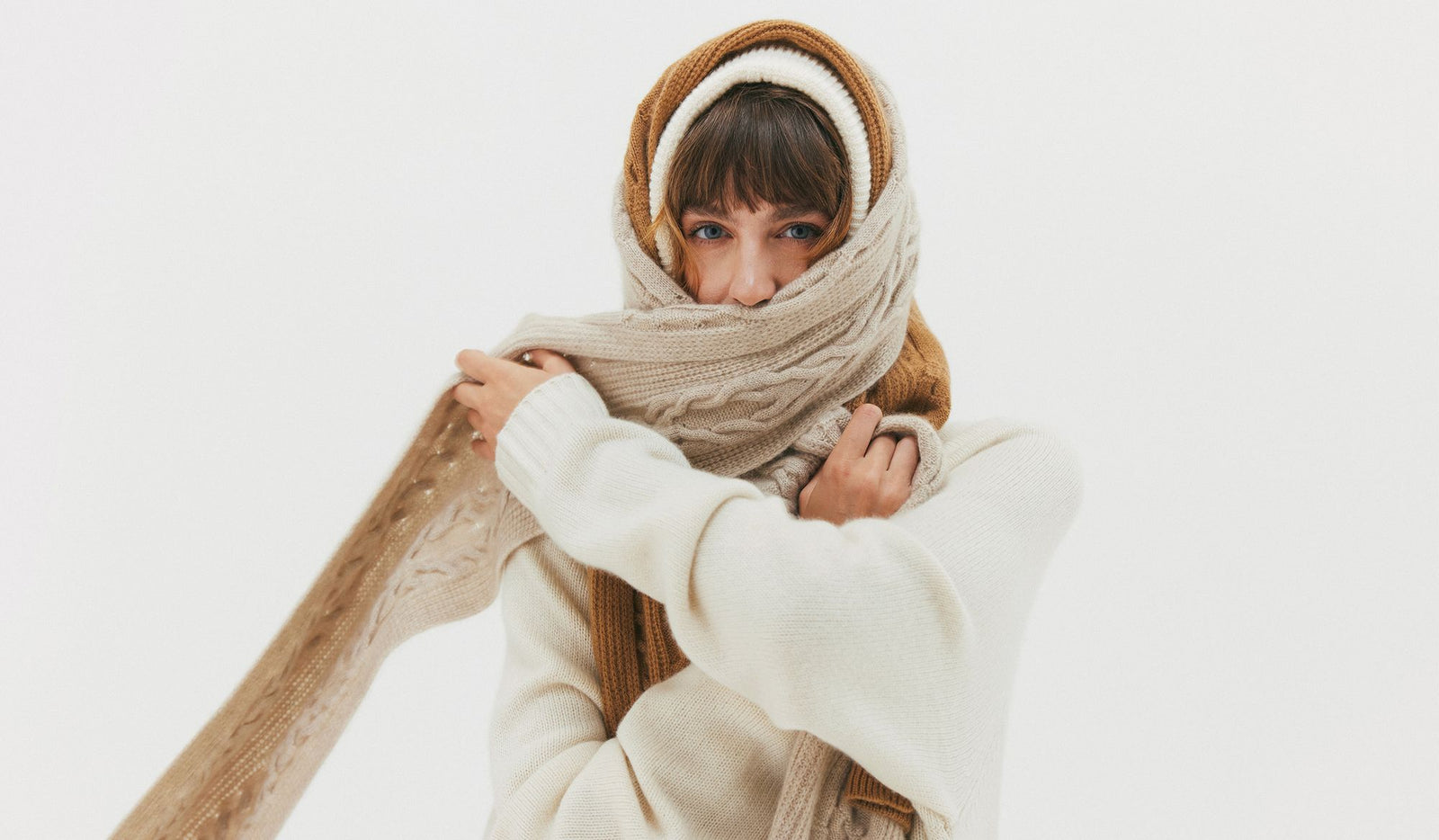 Woman wearing a beige scarf, brown headband, and white sweater on a light gray background