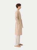 side view of Person wearing a beige trench coat on a white background #color_beige