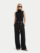 Woman wearing a black sleeveless turtleneck  top and wide-leg pants with a belt on a white background #color_black