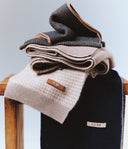 Stack of folded sweaters with 'Gobi' branding on a wooden chair against a light blue background