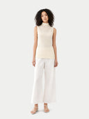 front view of Woman wearing a cream sleeveless top and white pants on a light gray background #color_marshmallow