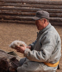 Man sitting on the ground holding a sheep's wool with stacked logs in the background