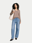 Woman wearing a brown sweater and blue jeans holding a beige tote bag on a white background #color_taupe