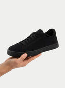 Black sneaker held in a hand against a white background #color_black