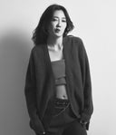 Black and white portrait of a person wearing a textured cardigan over a crop top and pants.