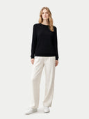 Woman wearing a black sweater and white pants on a white background #color_black