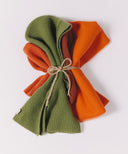 Two folded scarves, one green and one orange, tied together with twine on a white background.