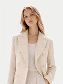 Close up of a woman wearing a beige blazer over a white top on a light background #color_beige