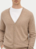 close up of a man wearing a beige v-neck cardigan with pockets over a white shirt on a light gray background #color_taupe