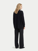 back view of a woman wearing a black cardigan and black pants on a white background #color_black
