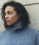 Woman wearing a blue turtleneck sweater against a neutral wall.