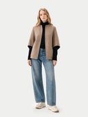 Woman wearing a beige crew neck coat, black turtleneck, blue jeans, and white sneakers on a white background #color_taupe #color_dark-navy