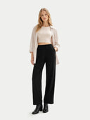 Woman wearing a beige top, black pants, and black boots on a white background #color_off-white