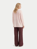 back view of a woman wearing a light pink sweater and dark brown pants on a white background #color_peach-blush