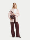 Woman holding a brown handbag wearing a light pink cardigan and dark red pants on a white background #color_peach-blush