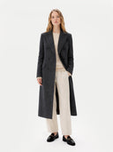 Woman wearing a long dark coat over a beige outfit on a white background #color_charcoal