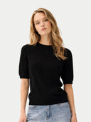 Woman wearing a black sweater and blue jeans on a light gray background #color_black