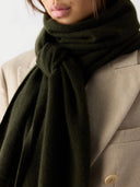 Close up of a person wearing a dark green scarf and beige coat #color_capulet-olive