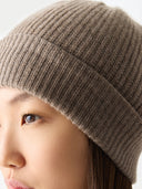 Close-up of a person wearing a brown knit beanie against a light background #color_taupe