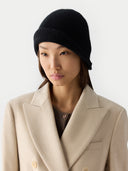 Woman wearing a black beanie and a beige coat against a white background #color_black