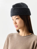 Woman wearing a dark gray knit beanie and beige sweater on a light gray background #color_charcaol