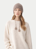Woman wearing a beige knit beanie with tassels on a white background #color_taupe