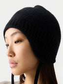 close up of a woman wearing a black beanie with ear flaps on a white background #color_black